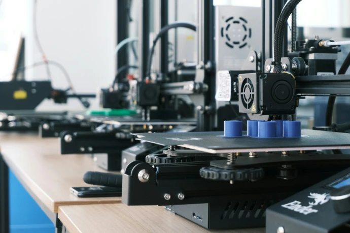 A row of 3D printers creating blue plastic cylinders on a wooden workbench